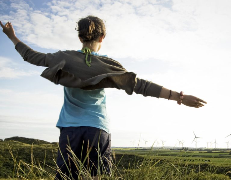 Our commitment to continuous improvement - child from behind running through a green field of wind turbines